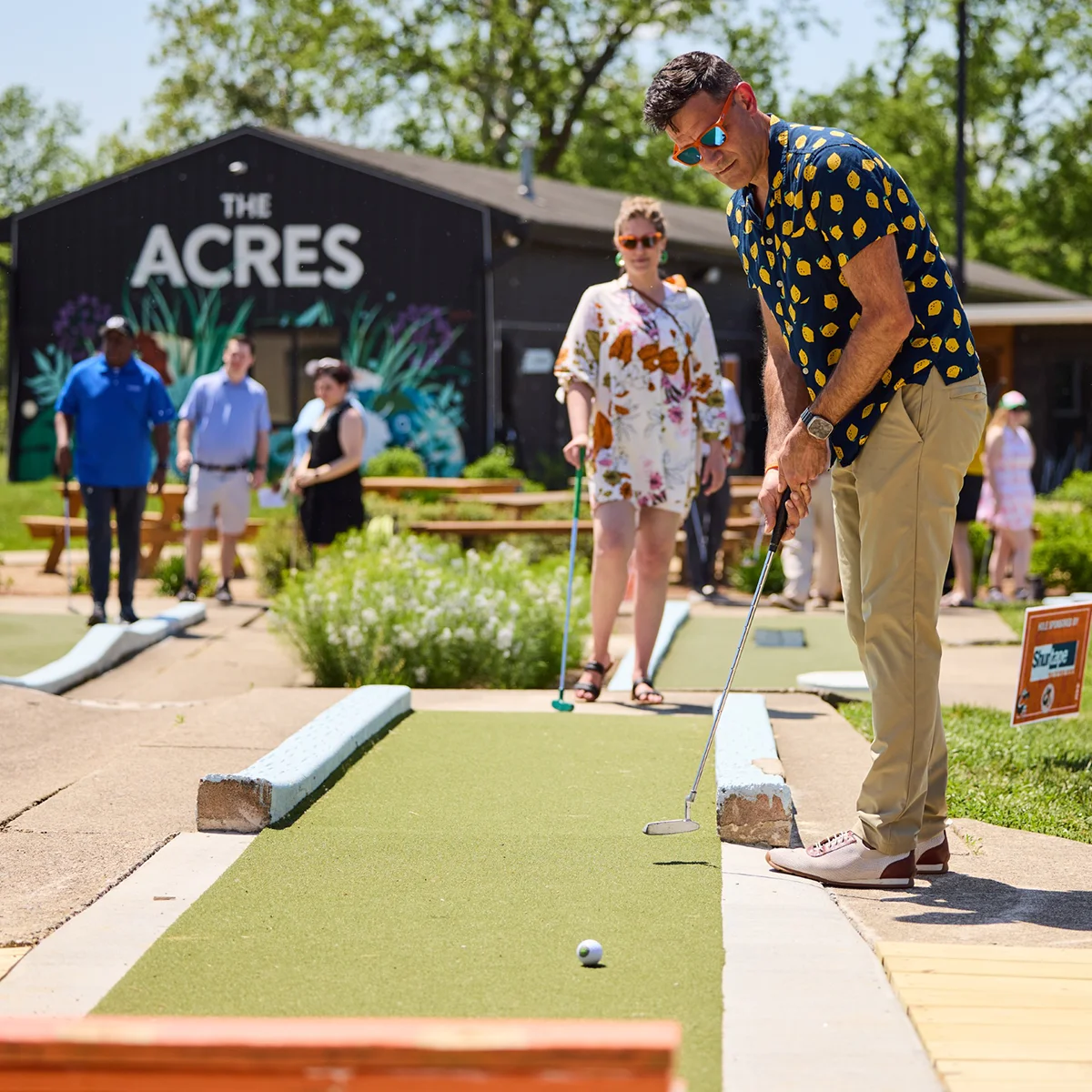 Friends playing mini golf in front of the painted ACRES barn at The Acres in Evendale